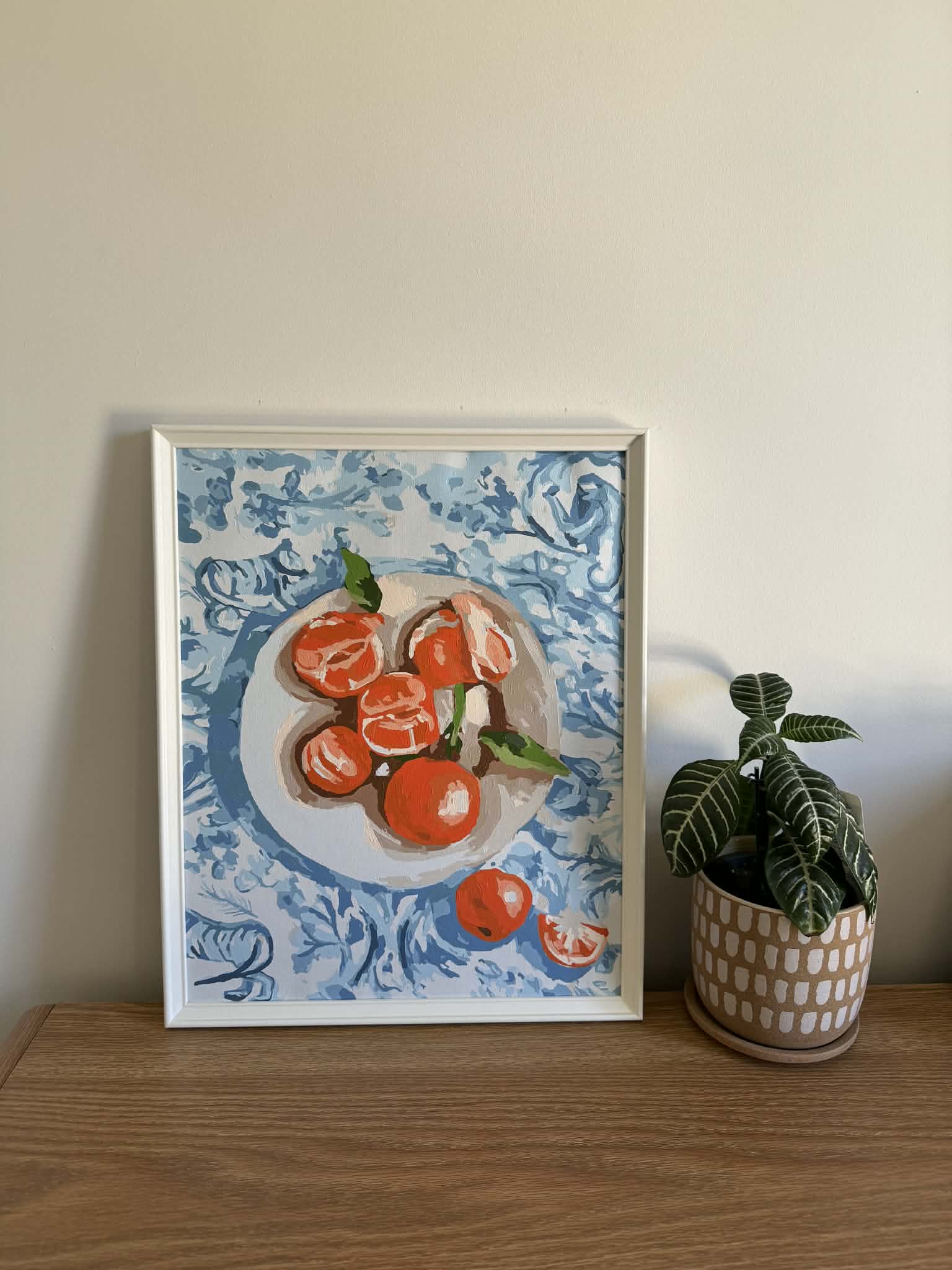 Framed painting of oranges on a blue patterned cloth